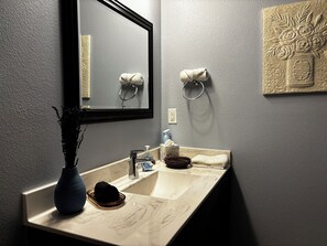 A bathroom with a marble sink, a mirror, a vase with a plant, a towel, and a decorative wall piece. - Splash pad, Pool, & Catch and Release Pond (Bixby)