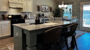 A kitchen with a central island, white cabinetry, and a dining area with chairs.