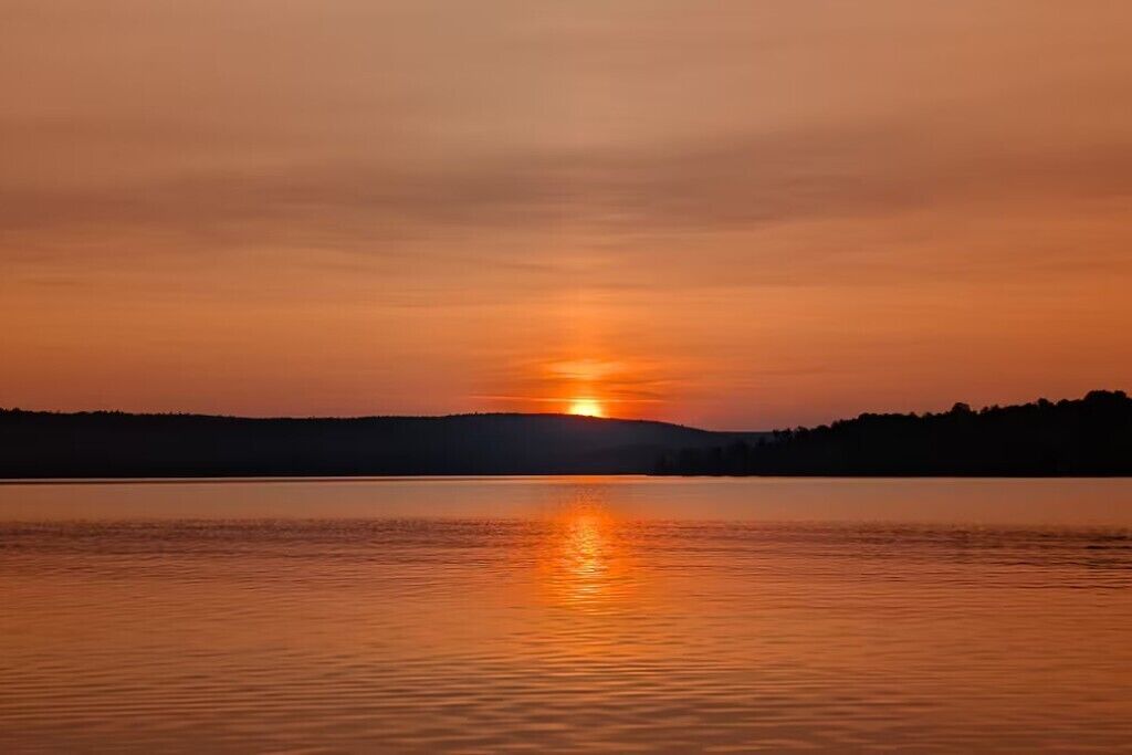 A sunset over a calm lake with a forested shoreline.