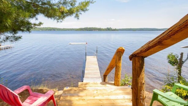 A wooden dock leading into a calm lake, with a red and a green chair on the dock. - Enjoy the Autumn colours on the edge of Algonquin park at Gramma's on the Lake (Barry's Bay)