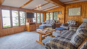 A cabin interior with wooden walls, large windows, a sofa set, a table, and a television. - Enjoy the Autumn colours on the edge of Algonquin park at Gramma's on the Lake (Barry's Bay)