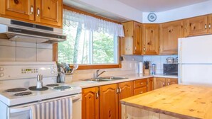 A kitchen with wooden cabinets, a white stove, and a window with a white valance. - Enjoy the Autumn colours on the edge of Algonquin park at Gramma's on the Lake (Barry's Bay)