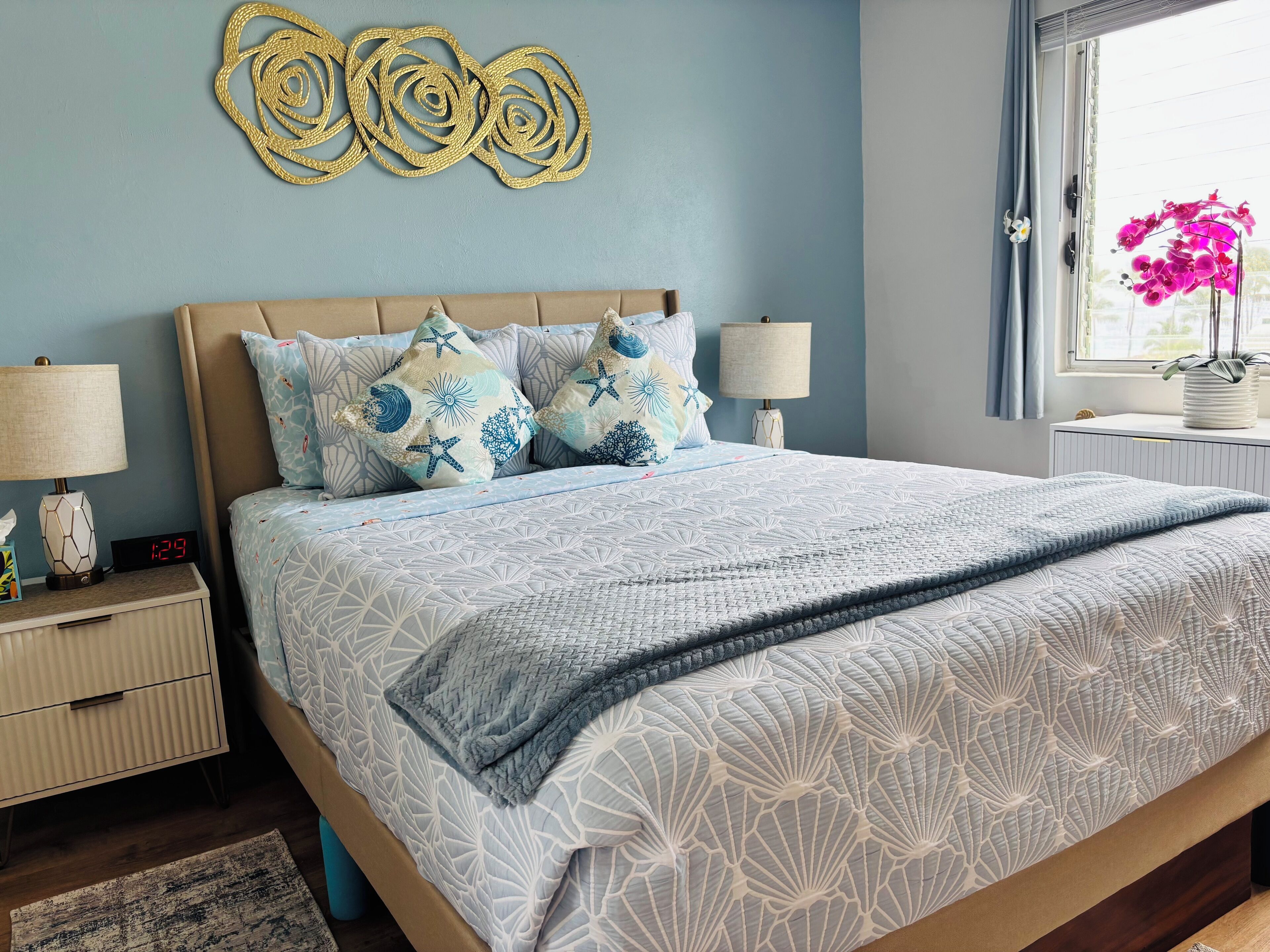 Ein ordentlich bezogenes Bett mit einer blau-weißen Bettdecke, passenden Kissen und einem dekorativen Wandbild.