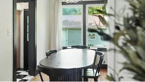 Comedor con una mesa redonda y sillas, una araña y vista a una casa a través de una ventana.
