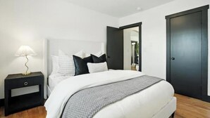 Un dormitorio con cama, mesita de noche, lámpara y puerta.