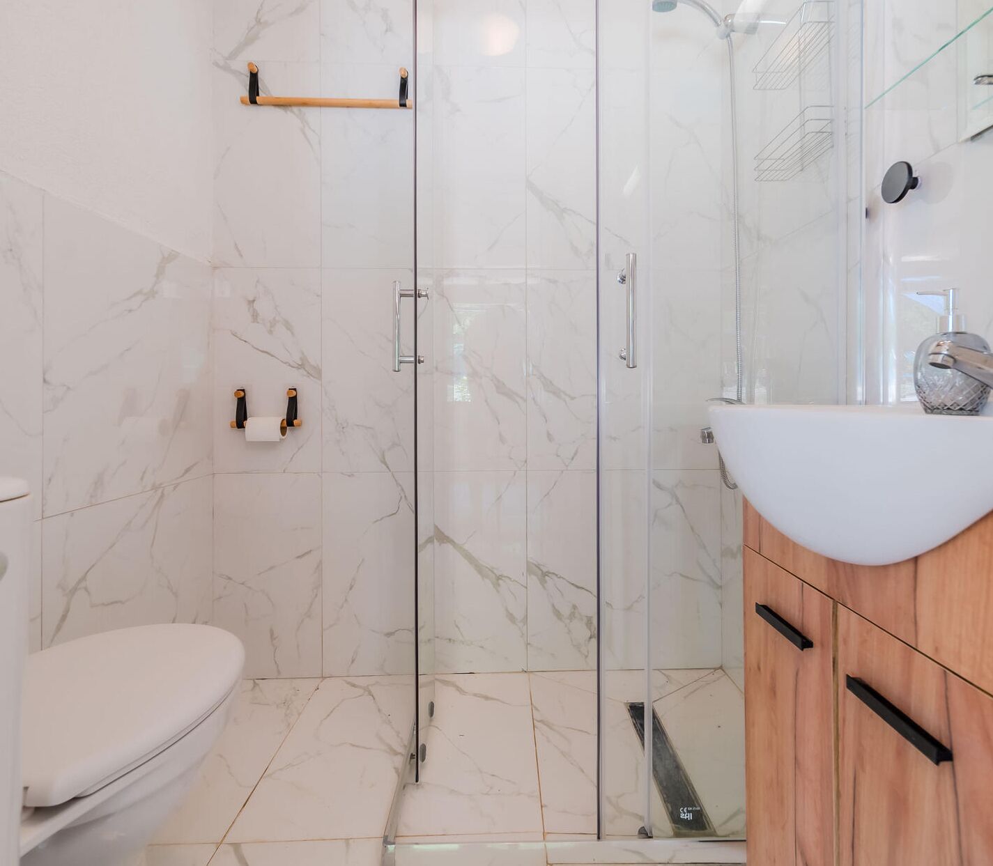 Un bagno con il water, una doccia con porta in vetro e un lavandino con mobiletto in legno.