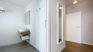 Une salle de bain moderne avec un plancher en bois, des murs blancs, un lavabo avec un miroir et une porte.