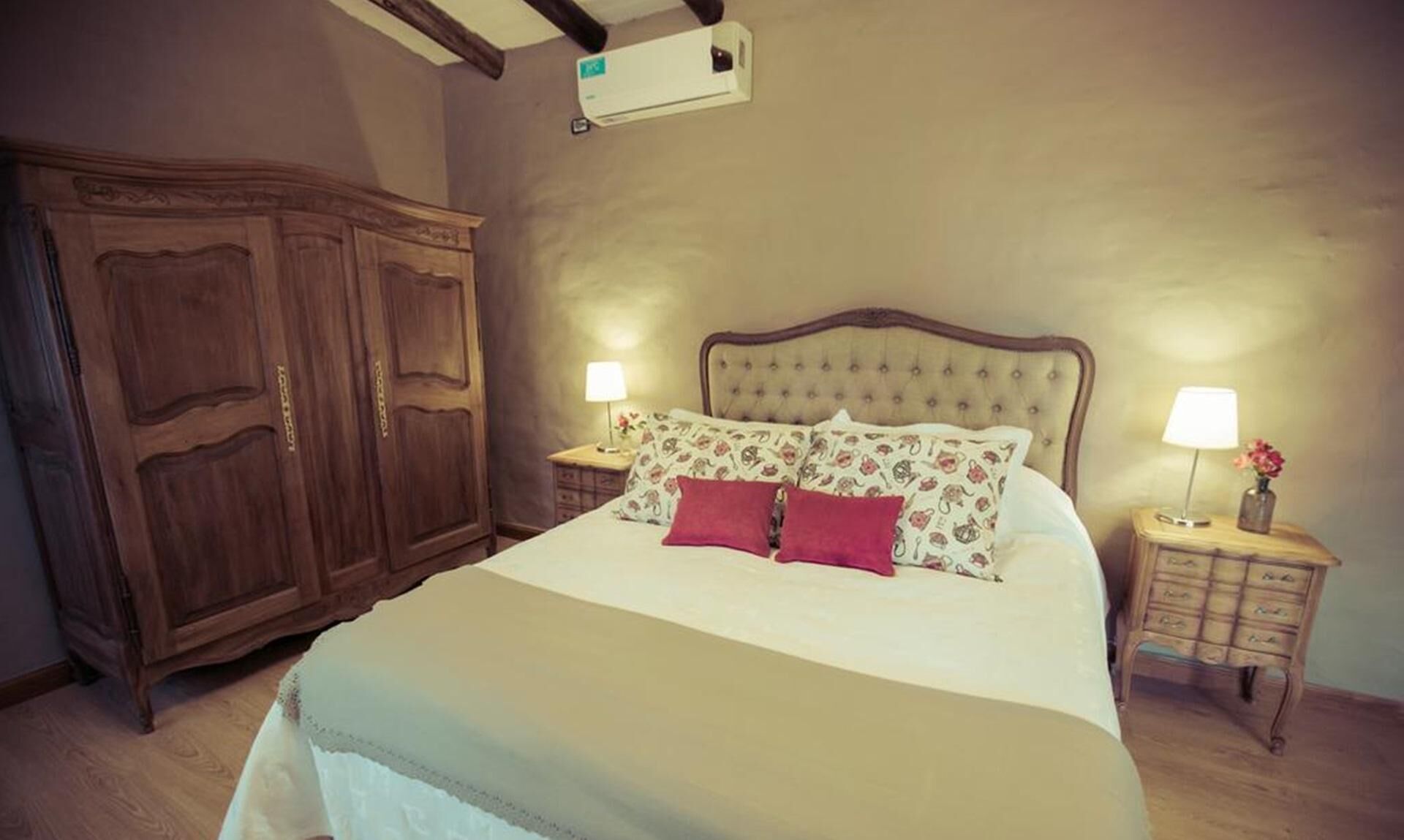 Un dormitorio con una cama grande, un armario de madera, mesitas de noche con lámparas y un aire acondicionado instalado en la pared.