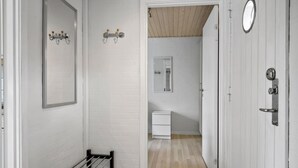 Un couloir doté d’un plancher en bois, une porte blanche ornée d’un miroir rond, et des toilettes blanches visibles à travers une porte entrouverte.