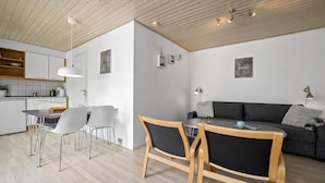 Une cuisine moderne avec des meubles blancs, un coin repas avec une table et des chaises, et un salon avec un canapé et une lampe fixée au mur.