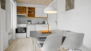 Une cuisine moderne avec des meubles blancs, un plafond en bois et un coin repas comprenant une table et des chaises.