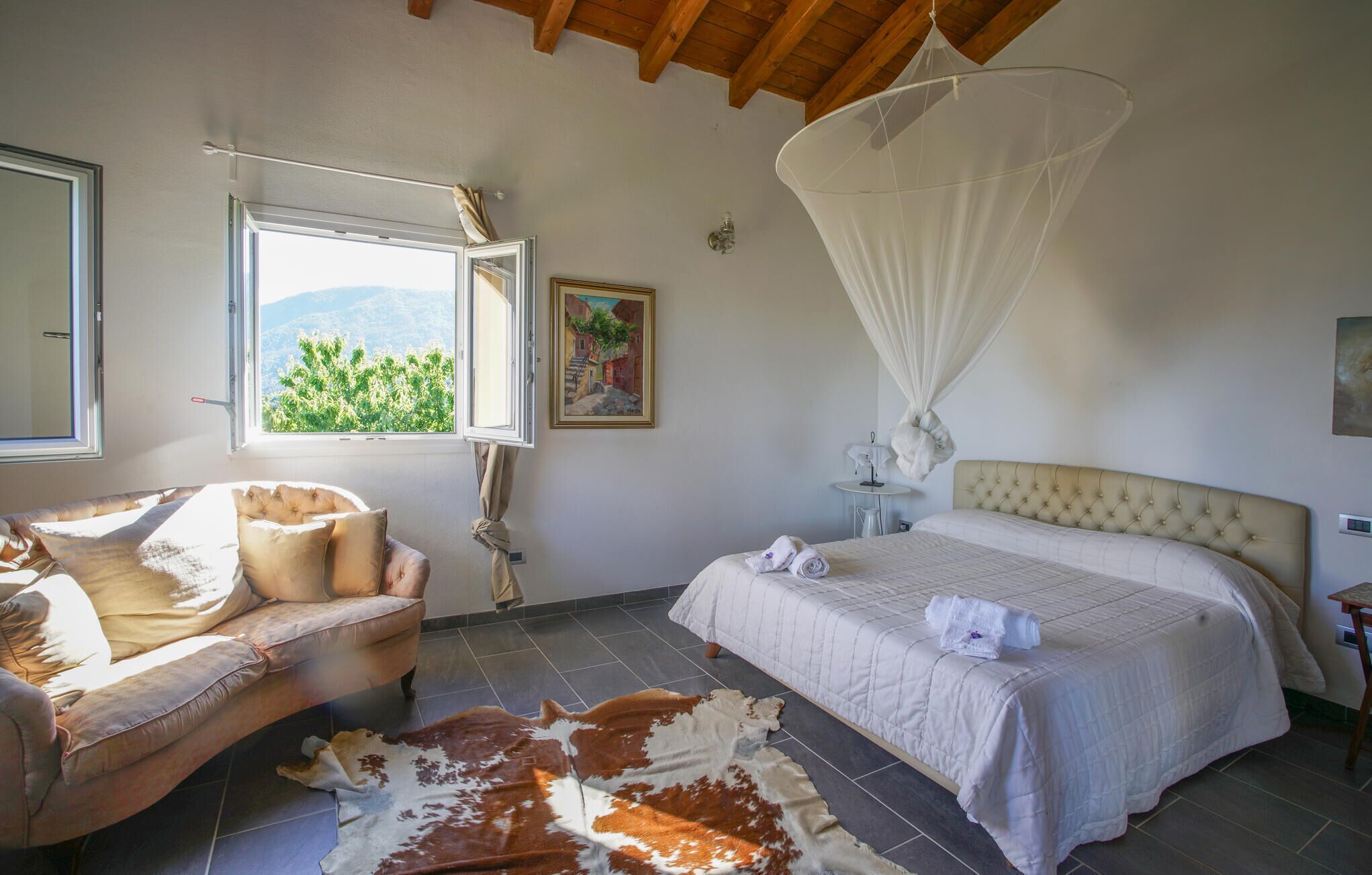 Ein Schlafzimmer mit Bett, Stuhl, Kuhfellteppich, Fenster mit Aussicht und Baldachin.