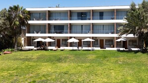 A multi-story hotel with a flat roof, large windows, and a well-maintained lawn with outdoor seating.
