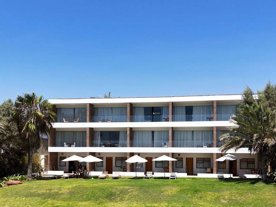 Un hotel de varios pisos con techo plano, ventanas amplias y un césped bien cuidado con mesas al aire libre.