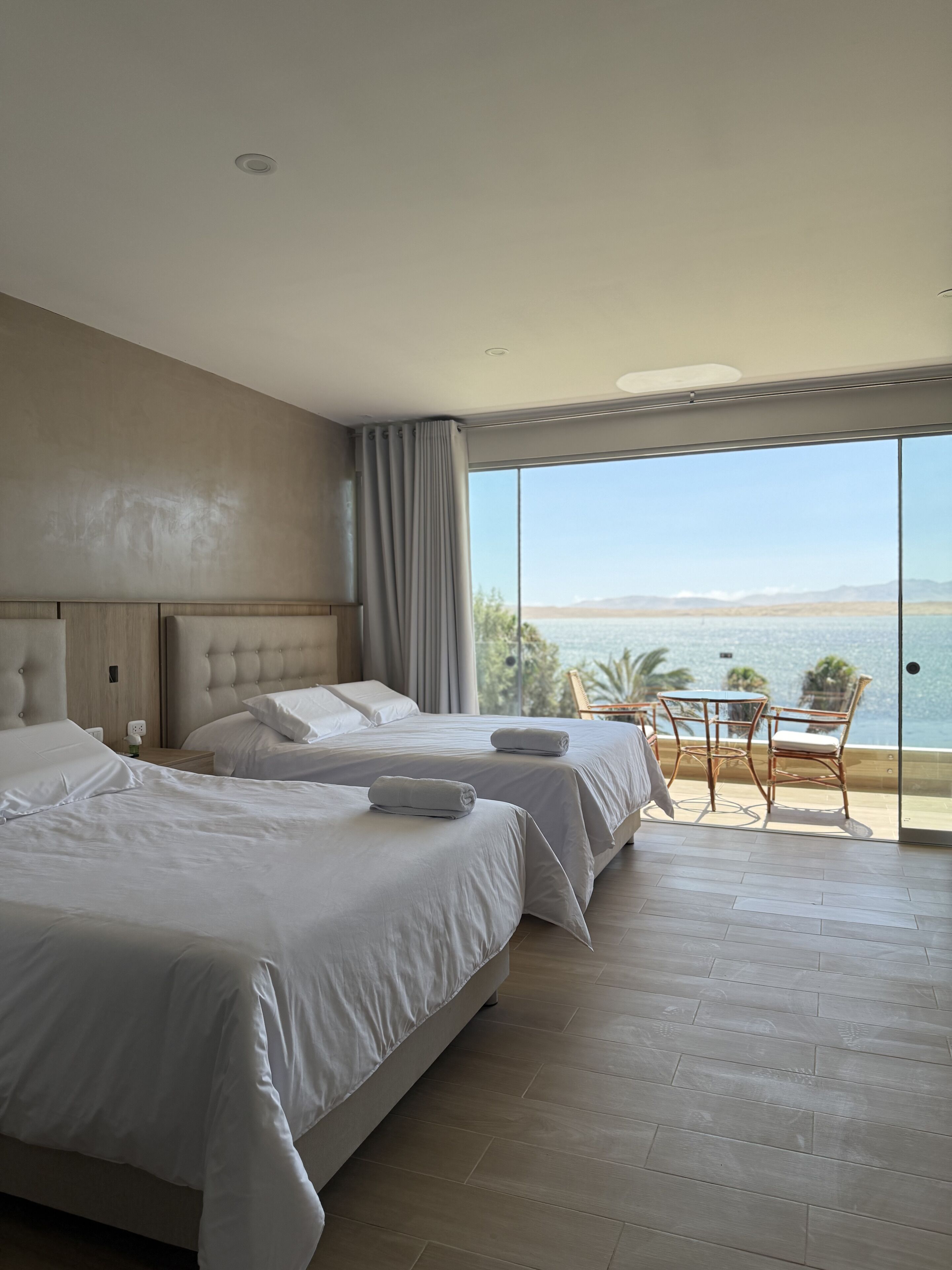 A hotel room with two beds, a balcony with a table and chairs, and a view of the sea.