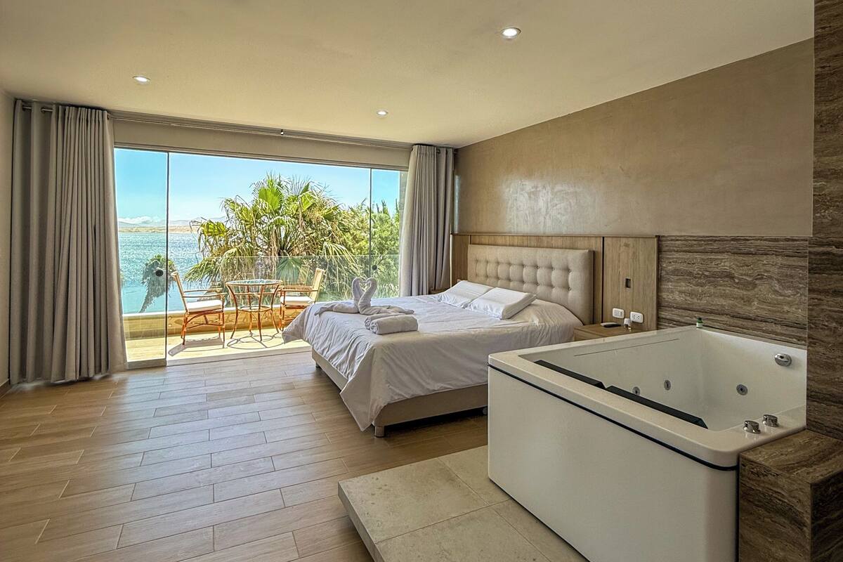A modern hotel room with a large bed, a separate sitting area with a view, and a standalone bathtub.