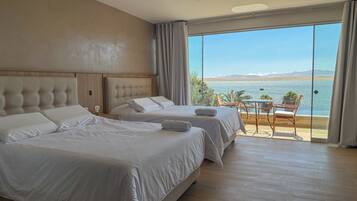 A hotel room with two beds, a balcony with a table and chairs, and a view of the sea.