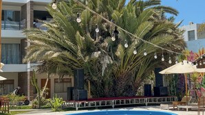 A pool area with a palm tree, lounge chairs, and a stage with speakers.