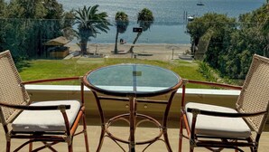 A balcony with wicker chairs and a glass table overlooking a beach and lake.