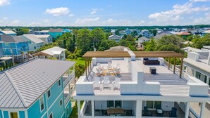 A residential area with a modern house featuring a rooftop deck with outdoor seating and a pergola.