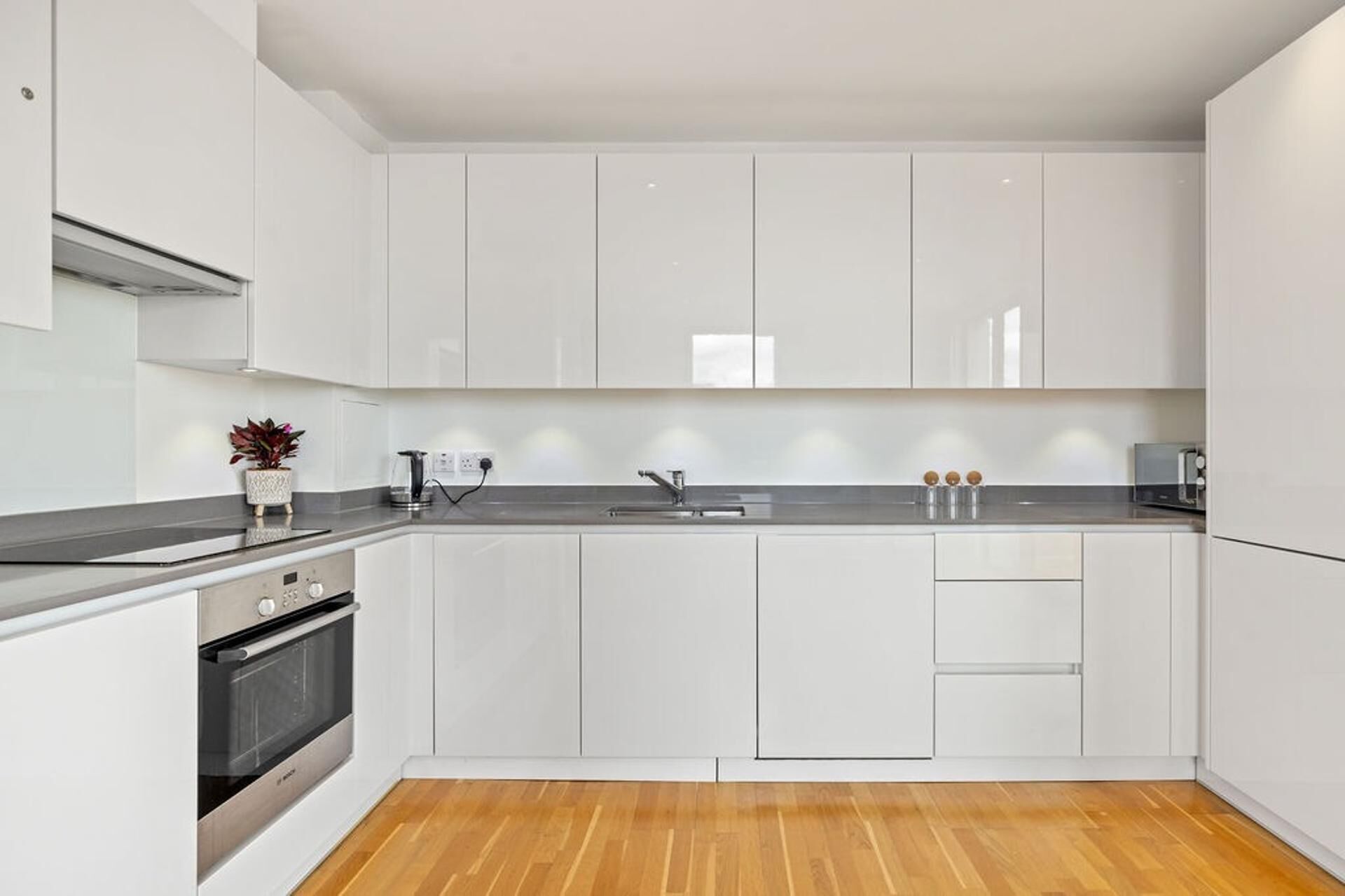 A modern kitchen with white cabinets, a stainless steel oven, a sink, and a countertop with a potted plant.