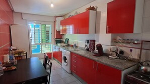 Una cocina compacta con armarios rojos y blancos, una lavadora, una mesa de comedor y una estufa.
