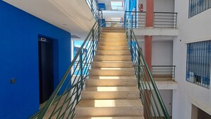 Un edificio de varios niveles con una escalera central, paredes azules y blancas y ventanas con barrotes.