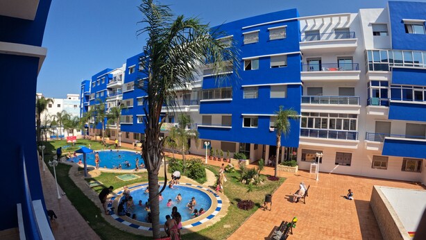 Un hotel de varios pisos con piscina rodeada de palmeras y un área de patio.