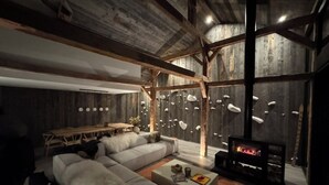 A modern living room with a fireplace, wooden beams, and a stone wall with hanging lights.