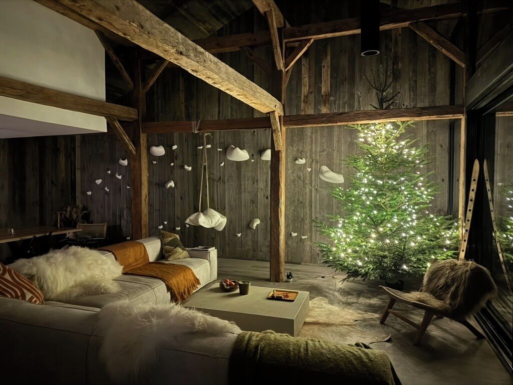 Ett mysigt vardagsrum med ett träpanelat tak, en soffa med fluffiga kuddar, ett soffbord och en julgran med ljus.