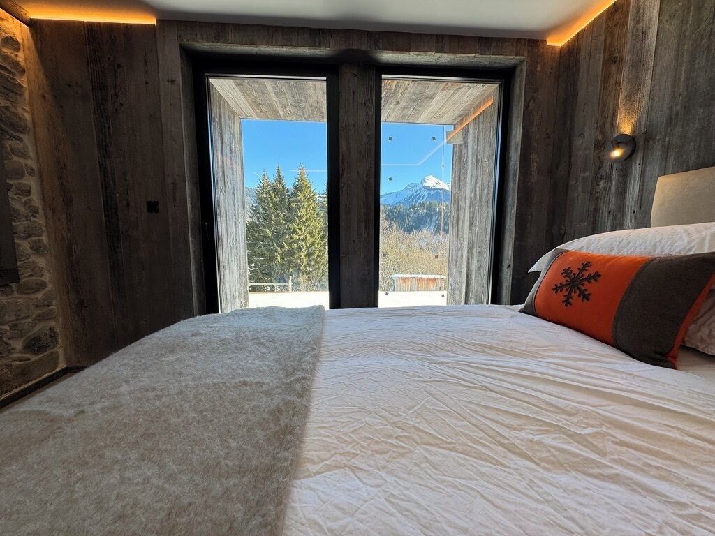 Ein Schlafzimmer mit einem großen Bett, einer Steinwand und Bergblick durch eine Glastür.