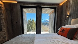 A bedroom with a large bed, a stone wall, and a view of mountains through a glass door.