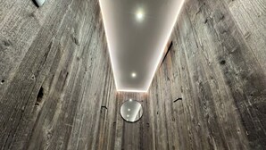 A narrow hallway with wooden walls and a polished floor, leading to a circular mirror on the far wall.