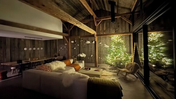 A cozy cabin interior with a wooden ceiling, a large window, a sofa, and a dining area.