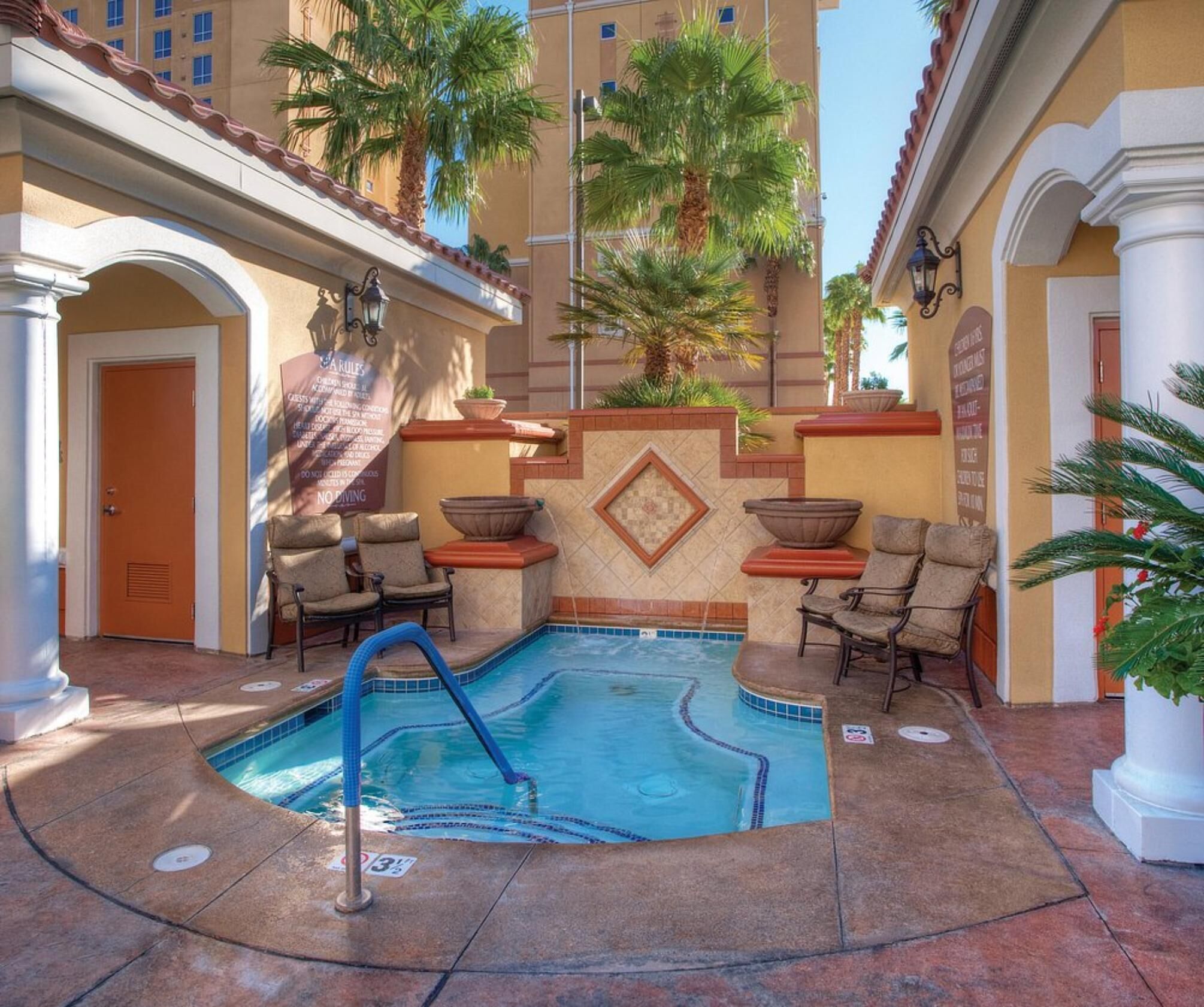 Un área de piscina con sillones reclinables, un jacuzzi y suelo de baldosas.