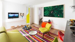 Een moderne woonkamer met een flatscreen televisie, een kleurrijk gestreept tapijt, een groene bank en een levendig schilderij aan de muur.