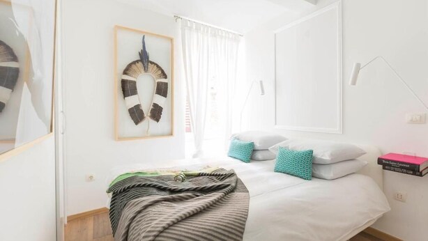 Een keurig opgemaakt bed met een gestreept dekbedovertrek, een aan de muur hangend kunstwerk en een bedlampje.