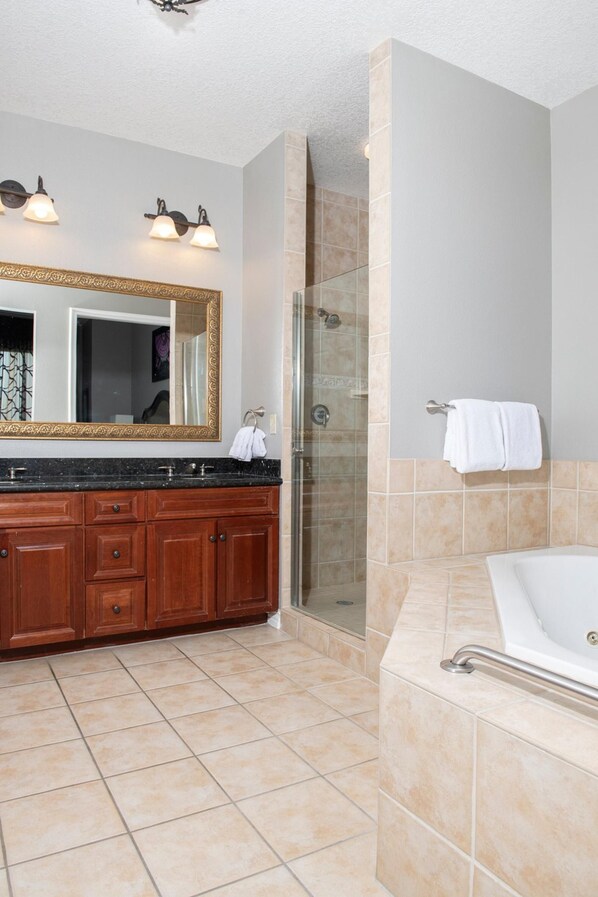 A bathroom with a large mirror, a bathtub, a shower area, and a vanity with a sink.