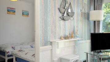 Un dormitorio con cama, televisión, una mesita blanca y una ventana con cortinas.