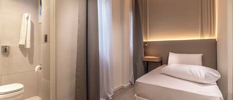 A modern hotel room with a toilet, a bed with white bedding, and a nightstand.