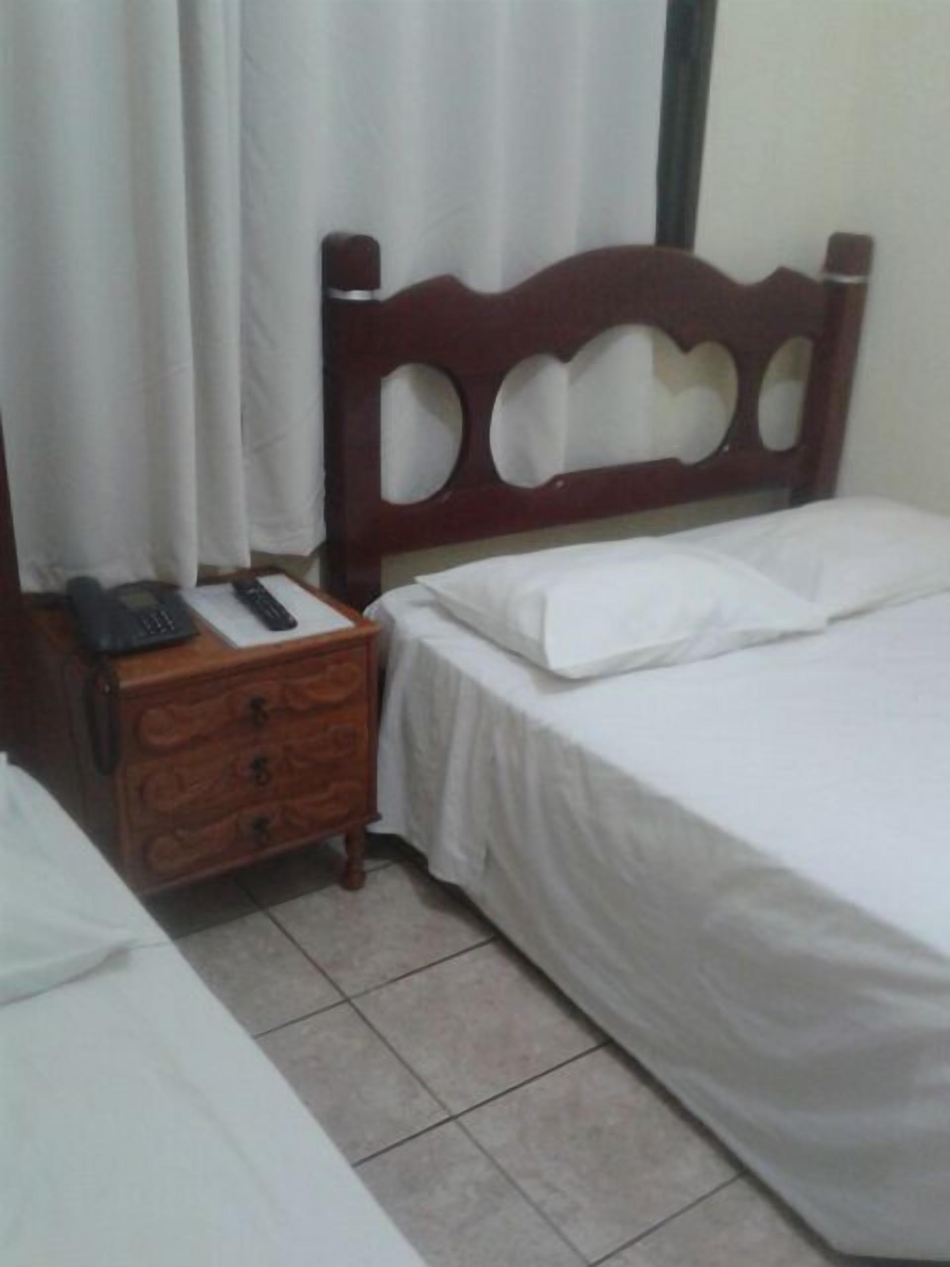 Une chambre à coucher avec une tête de lit en bois, une table de chevet avec un téléphone et un lit recouvert de draps blancs.