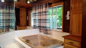 A bathroom with a large bathtub, wooden cabinets, and a window with curtains.