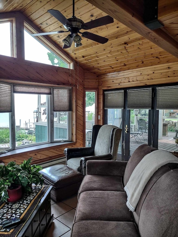 A wooden interior with a ceiling fan, large windows with blinds, a leather sofa, and a potted plant.