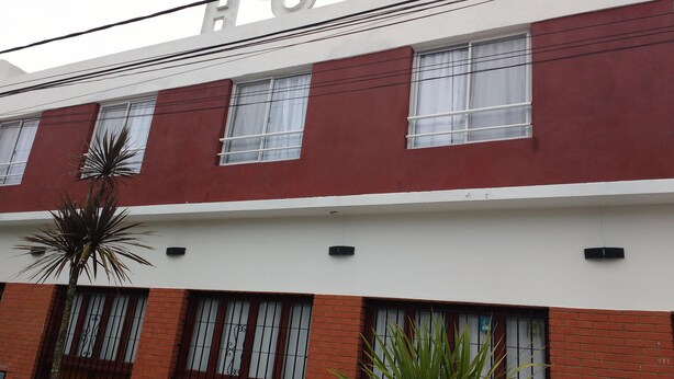 A building with a red and white facade, multiple windows with metal bars, and a visible door. - Hotel Mar de Ajo (Mar de Ajo)