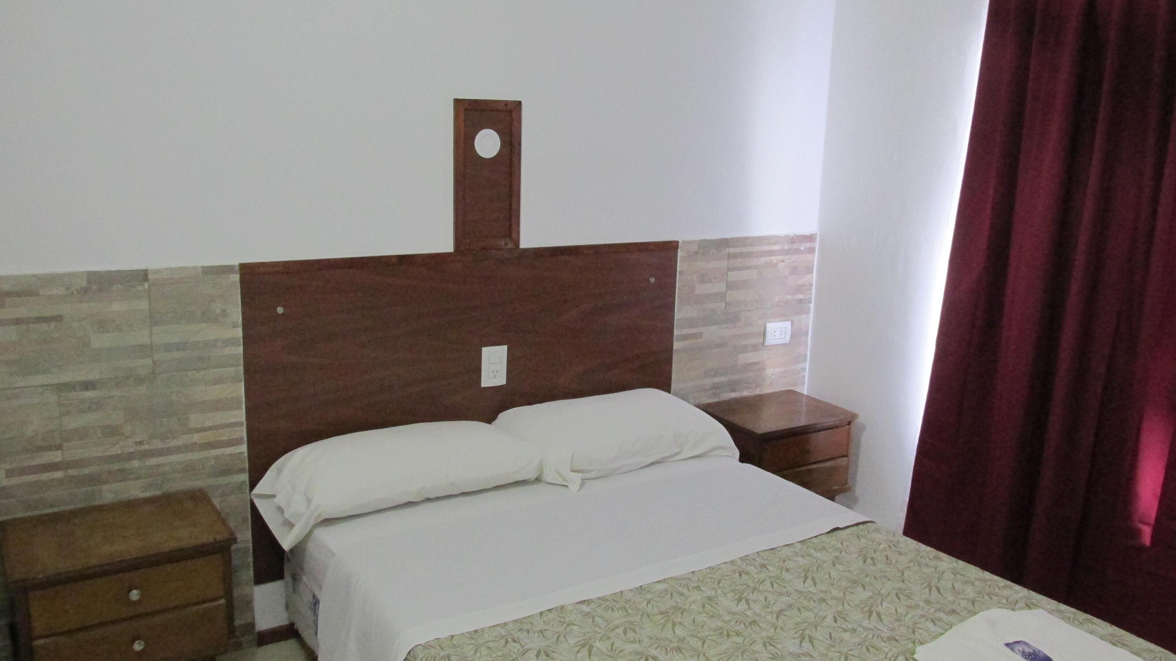 Una cama individual con cabecera de madera, dos mesitas de noche y una colcha estampada.