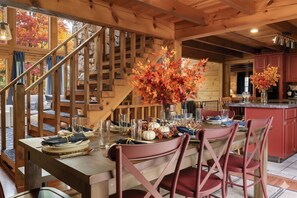Un interior de madera con una mesa de comedor preparada para cuatro personas, una escalera y una zona de cocina.