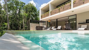 Un espace piscine moderne avec une piscine à eau claire, des chaises longues et un bâtiment doté de grandes fenêtres et de plantes sur le balcon.