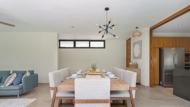 Un espace repas moderne avec une table en bois, des chaises à revêtement gris et un luminaire central.