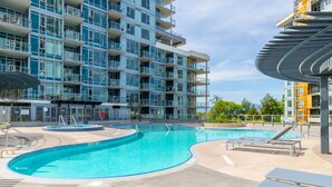 A modern apartment building with a swimming pool and sun loungers. - Lakeside Retreat w/ Rooftop Pool, Hot Tub, Firepits & BBQs – 10 min to Downtown (Kelowna)
