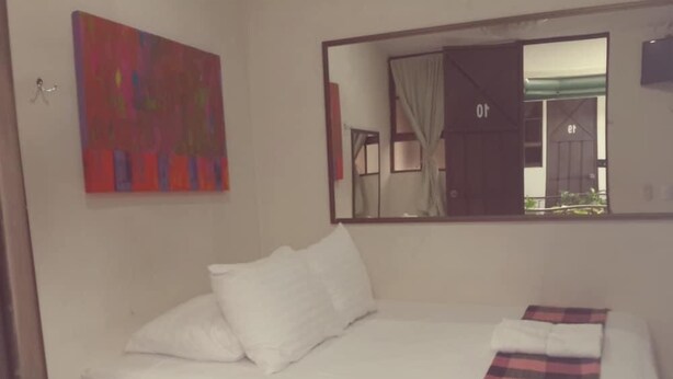 A bed with white bedding, a plaid blanket, and a mirror above it. - Hotel San Juan de León (León)